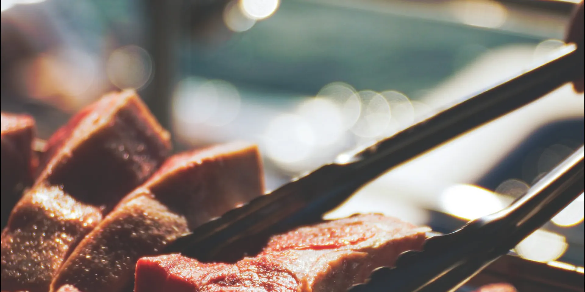 Chargrilled meat being turned on tongs, close up