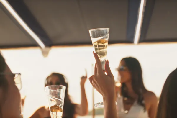 A guest raising a glass of sparkling wine on Bote at golden hour